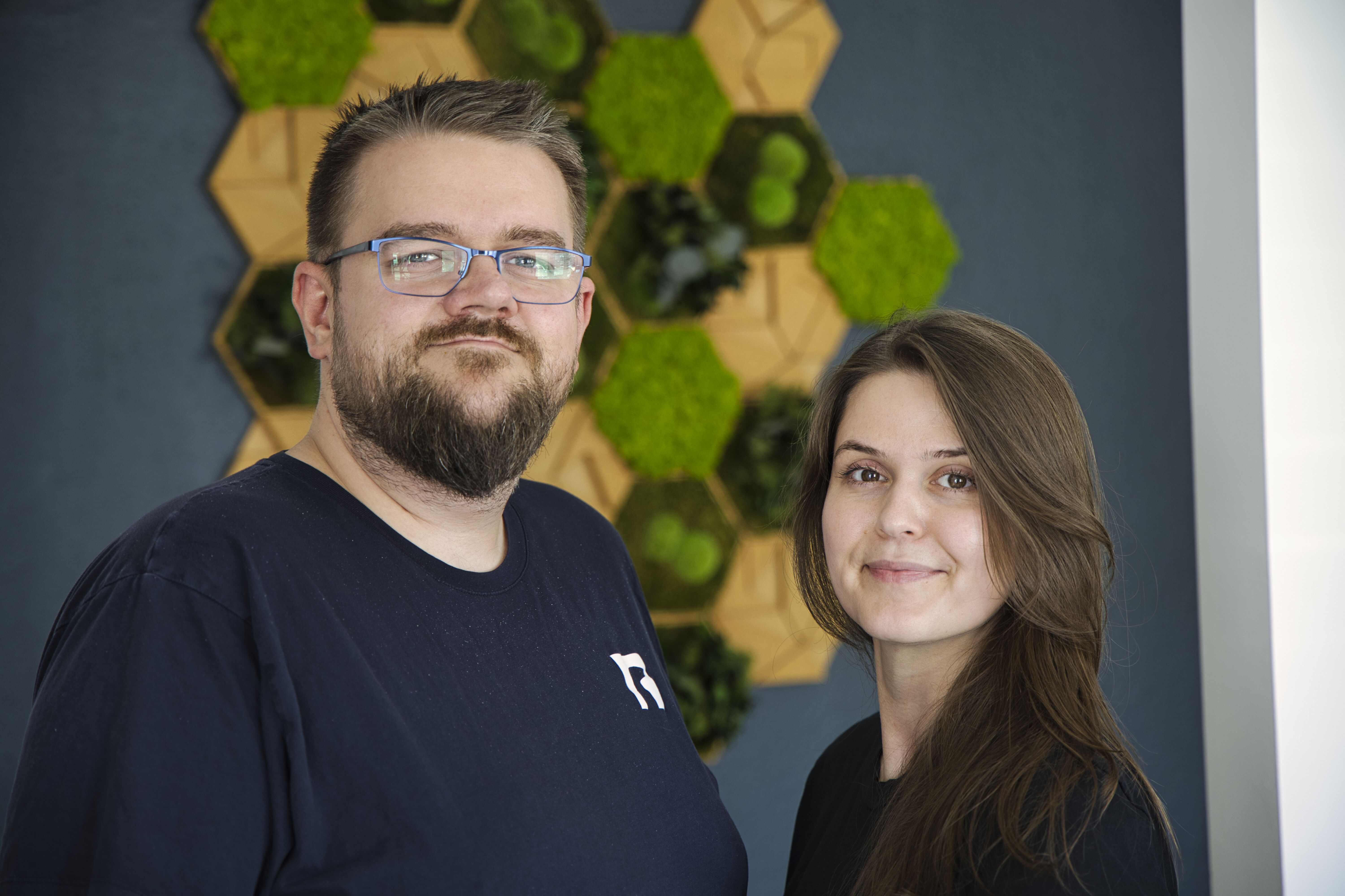 Zwei Teammitglieder von Systemhaus Erdmann vor der Hexagon-Mooswand